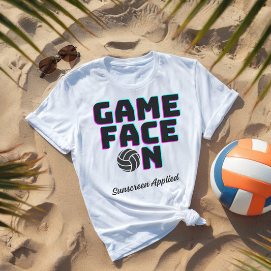 White t-shirt with 'GAME FACE ON Sunscreen Applied' text on a sandy background with a volleyball and sunglasses.